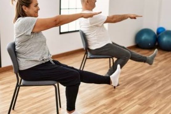 Middle age hispanic couple stretching using chair at sport center.